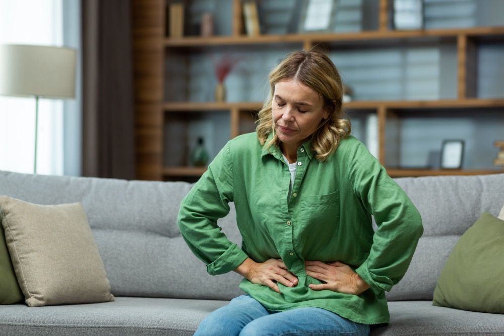 Frau sitzt auf dem Sofa und hat Schmerzen im Unterleib