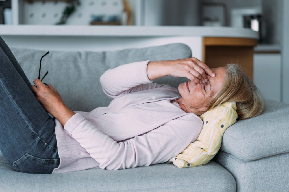 Frau liegt auf dem Sofa und fasst sich an den Kopf